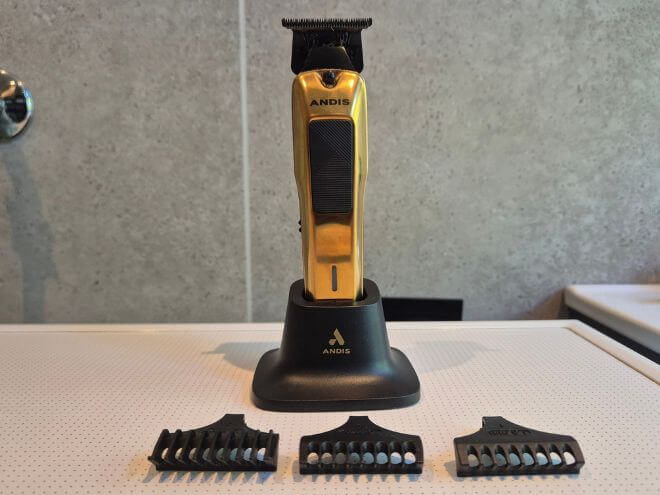 Andis Phenom trimmer i gull står i ladestativet, med de tre avstandskammene på 1,5, 3 og 6 mm